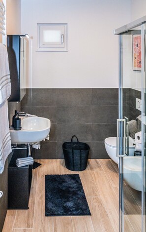 A modern bathroom with a white sink, a glass shower enclosure, and a black rug on the floor. - Art&Fashion- Ariom Apartments (Moniga del Garda)