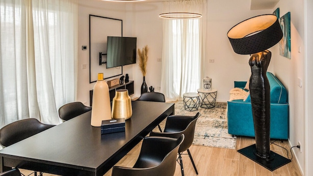 Ein modernes Wohnzimmer mit Essbereich, einem flachbildfernseher an der Wand, einer großen Stehlampe und einem blauen Sofa.