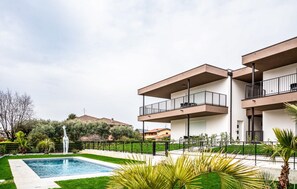 Un edificio moderno de dos pisos con balcones, piscina y follaje circundante.