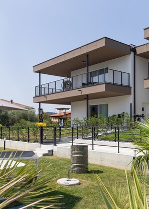 A modern multi-story building with balconies, a paved area with plants, and a clear sky. - Jungle Lake - Ariom Apartments (Moniga del Garda)