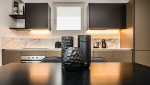 Une cuisine moderne avec des meubles de couleur sombre, un plan de travail en marbre et un îlot central agrémenté de deux vases décoratifs.