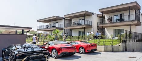 A parking area with three sports cars, a modern building with balconies, and a clear sky.