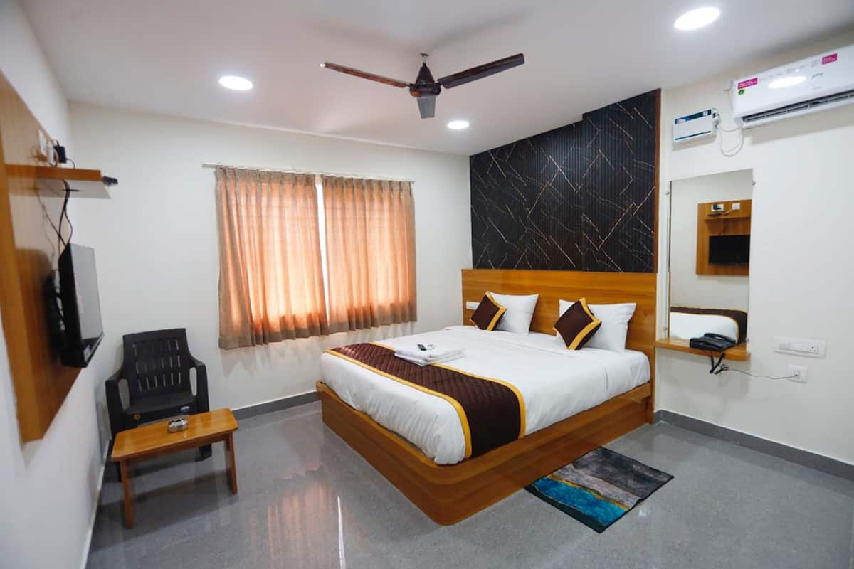 A hotel room with a bed, a ceiling fan, an air conditioning unit, a television, a desk, and a chair.