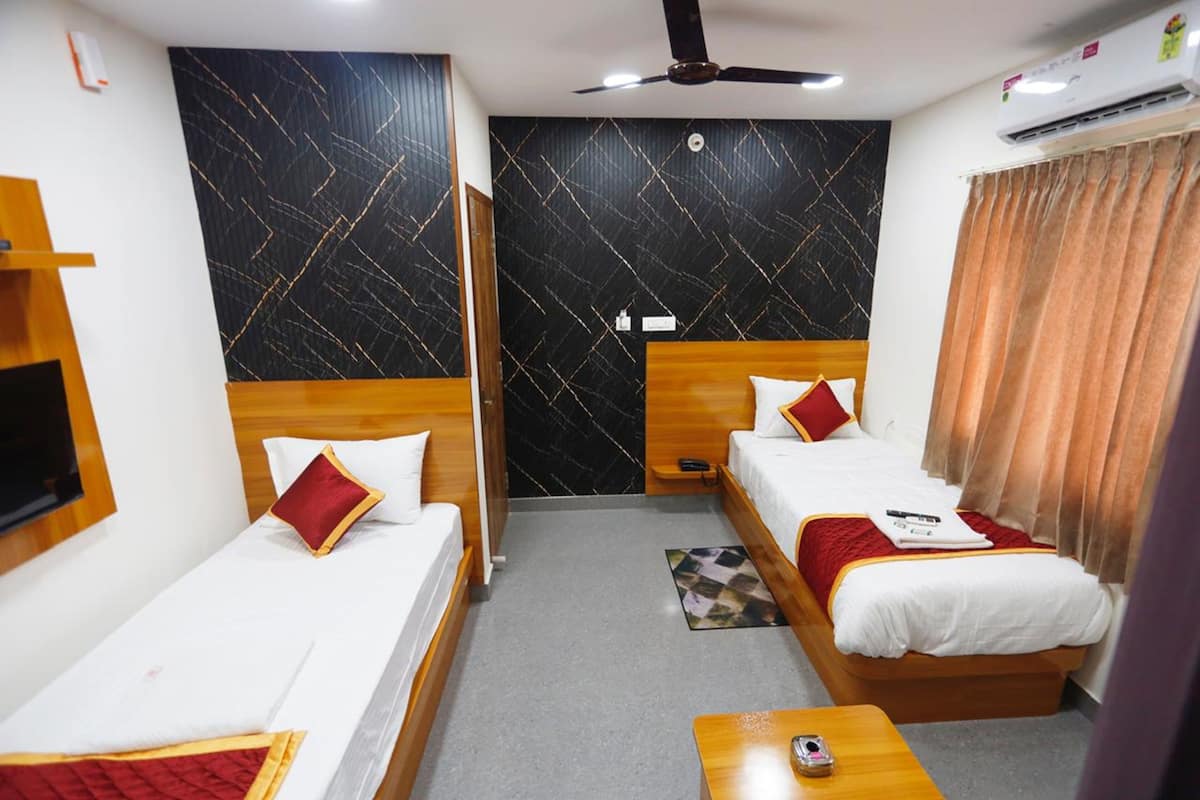 A hotel room with two single beds, a wooden headboard, a small table, a ceiling fan, and an air conditioning unit.