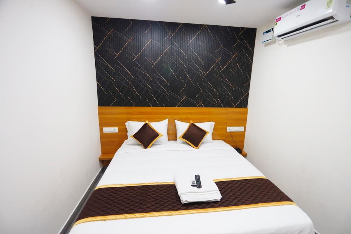 A hotel room with a bed, a headboard, a wall-mounted air conditioner, and a remote control on the bed.