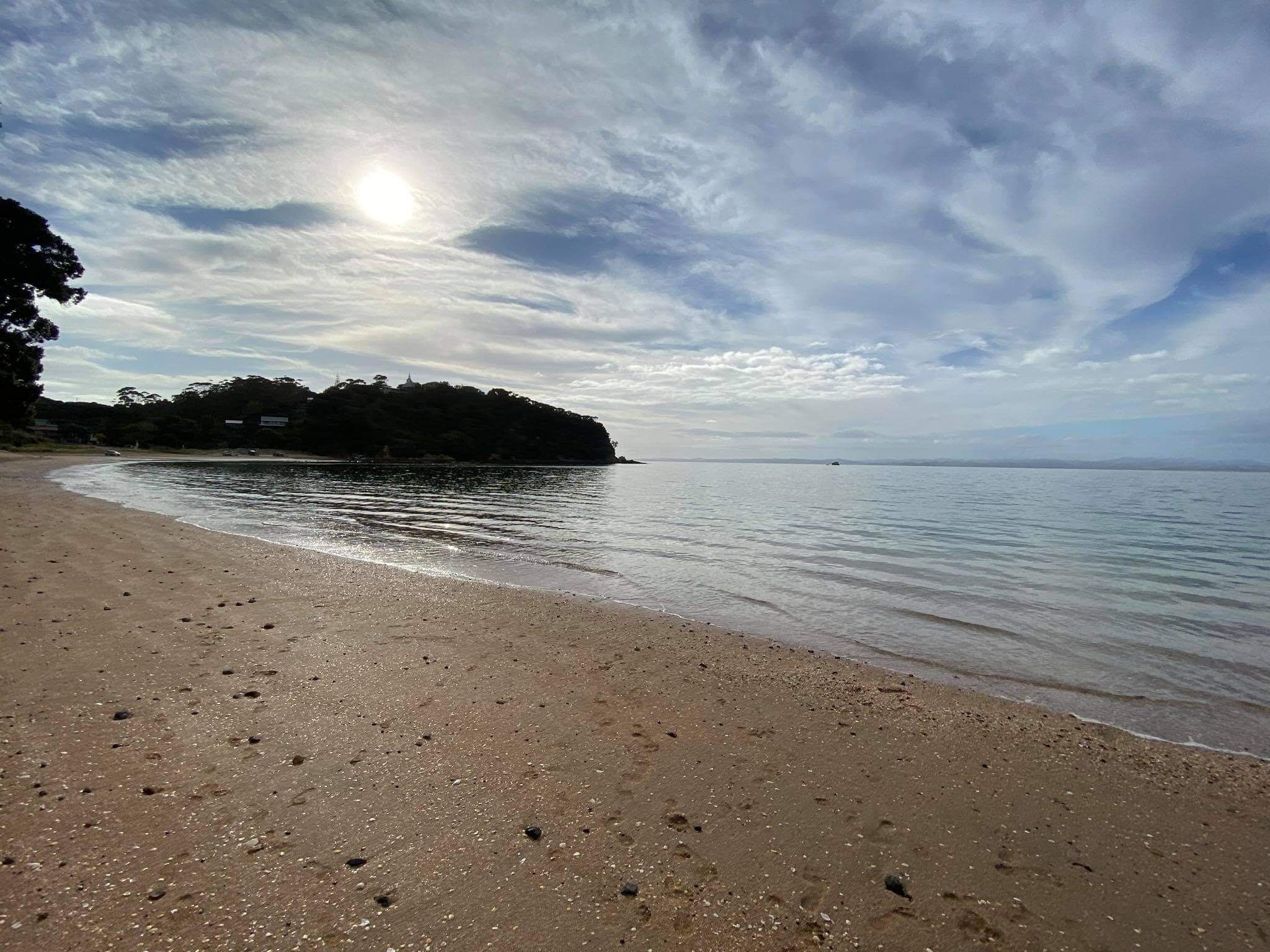 Une plage avec un ciel dégagé, une eau calme et une terre ferme visible au loin.