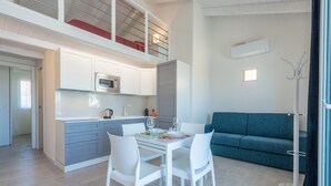 A modern kitchen with white cabinets, a dining table with chairs, a blue sofa, and a coat rack. - Affittimoderni Castelsardo - Blue Loft (Castelsardo)