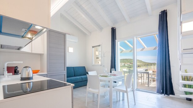 A modern kitchen with a built-in stove, a dining area with a table and chairs, a blue sofa, and a view through a glass door to the outdoors. - Affittimoderni Castelsardo - Blue Loft (Castelsardo)