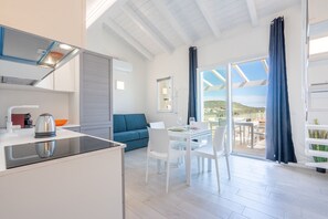 Eine moderne Küche mit eingebautem Herd, ein Essbereich mit Tisch und Stühlen, ein blaues Sofa und ein Blick ins Freie durch eine Glastür.