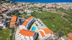 An aerial view of a coastal residential area with a prominent building featuring a swimming pool and a curved roof. - Affittimoderni Castelsardo - Blue Loft (Castelsardo)