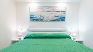 A bedroom with a bed, green bedding, a painting of sailboats on water, and two bedside lamps. - Affittimoderni Castelsardo - Blue Loft (Castelsardo)