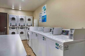 Une buanderie équipée de plusieurs machines à laver et de plusieurs sèche-linge, d’un panneau de commande et d’affiches informatives sur les murs.