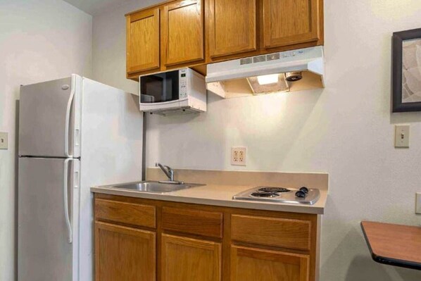 Una cocina compacta con armarios de madera, un refrigerador blanco, un microondas y una estufa a gas.