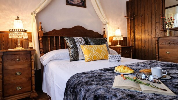 A bedroom with a four-poster bed, wooden nightstands, a chandelier, and a bedside table with a lamp.