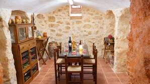 A stone-walled dining area with a wooden table and chairs, a wine cabinet, and a small window.