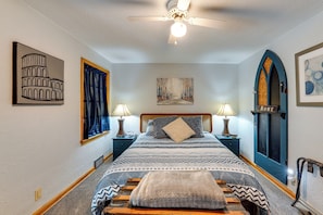 A bedroom with a bed, two bedside tables with lamps, a ceiling fan, artwork on the walls, and a door labeled 'ROME'. - 1 Mi to Dtwn Tiffin! Brick Bungalow w/ Patio, Yard (Tiffin)