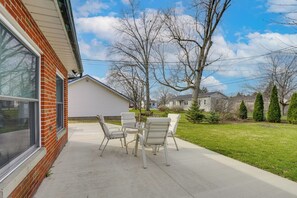 A patio with a table and chairs, a brick building, and a lawn with trees. - 1 Mi to Dtwn Tiffin! Brick Bungalow w/ Patio, Yard (Tiffin)
