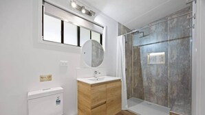 A modern bathroom with a toilet, sink, mirror, and shower. - Agnes Bush Cabins #3 (Round Hill)