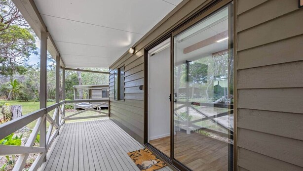 A covered porch with a wooden deck, a glass door leading to a backyard, and a small rug on the deck. - Agnes Bush Cabins #3 (Round Hill)