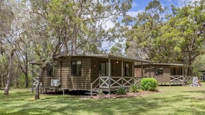 A single-story wooden cabin with a porch, surrounded by trees and grass. - Agnes Bush Cabins #3 (Round Hill)