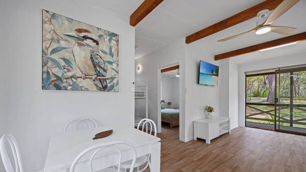 A spacious room with a dining table, chairs, a ceiling fan, a painting, a TV, and a sliding glass door leading to an outdoor area. - Agnes Bush Cabins #4 (Round Hill)