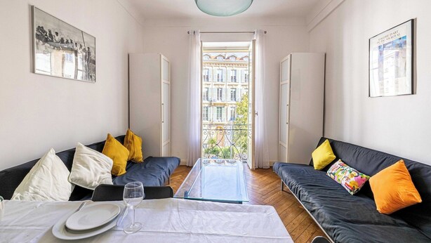 A modern living room with a sofa set, a dining table with a glass top, and a view of a building through a door. - Warm Apartment 2P in the heart of Nice - near the sea (Nice)