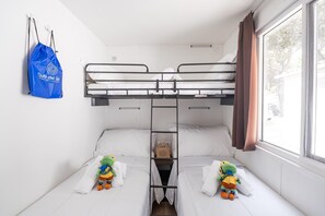 Une chambre avec un lit superposé, une fenêtre, un sac bleu et deux peluches.