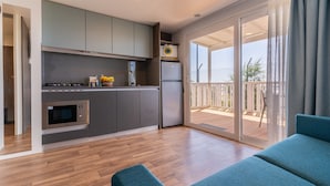 A modern kitchen with grey cabinets, a built-in oven, and a refrigerator. There is a sliding glass door leading to a balcony with a wooden deck. - Jesolo Family Resort (Lido de Jesolo)