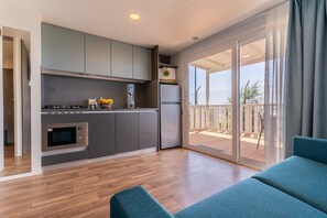 A modern kitchen with grey cabinets, a built-in oven, and a refrigerator. There is a sliding glass door leading to a balcony with a wooden deck. - Jesolo Family Resort (Lido de Jesolo)