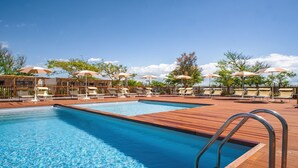 Une piscine entourée d’une terrasse en bois et d’arbres, avec des chaises longues et des parasols à proximité.