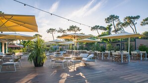 Une terrasse extérieure dotée d’un plancher en bois, de plusieurs tables et chaises, et de grands parasols offrant de l’ombre.