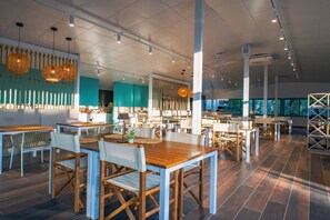 Un restaurant spacieux avec des tables et des chaises en bois, des luminaires suspendus et un design de plafond moderne.