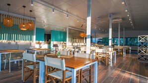 Un'ampia sala ristorante con tavoli e sedie in legno, lampade a sospensione e un moderno design del soffitto.
