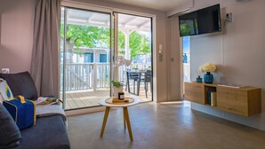 Un soggiorno moderno con un divano, un tavolino rotondo, una TV a parete e una porta scorrevole in vetro che dà su un balcone esterno.