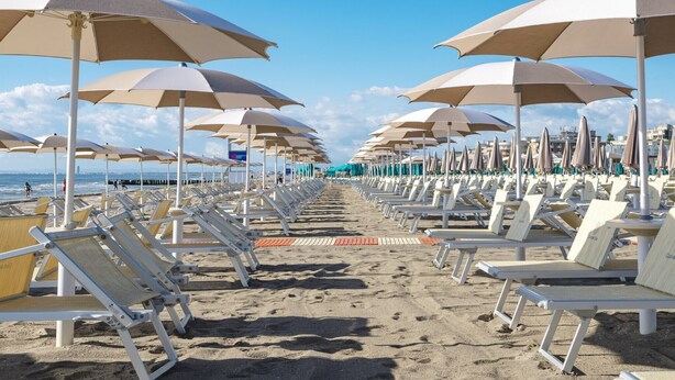 Una spiaggia con file di lettini e ombrelloni, cielo sereno e vista sullo sfondo del mare.