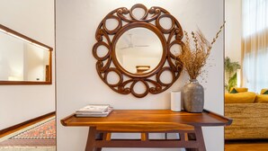 A wooden console table with a mirror, a vase with dried plants, and a magazine. - Alara by Alaya Stays 4-BHK Apartment (Kanayannur)