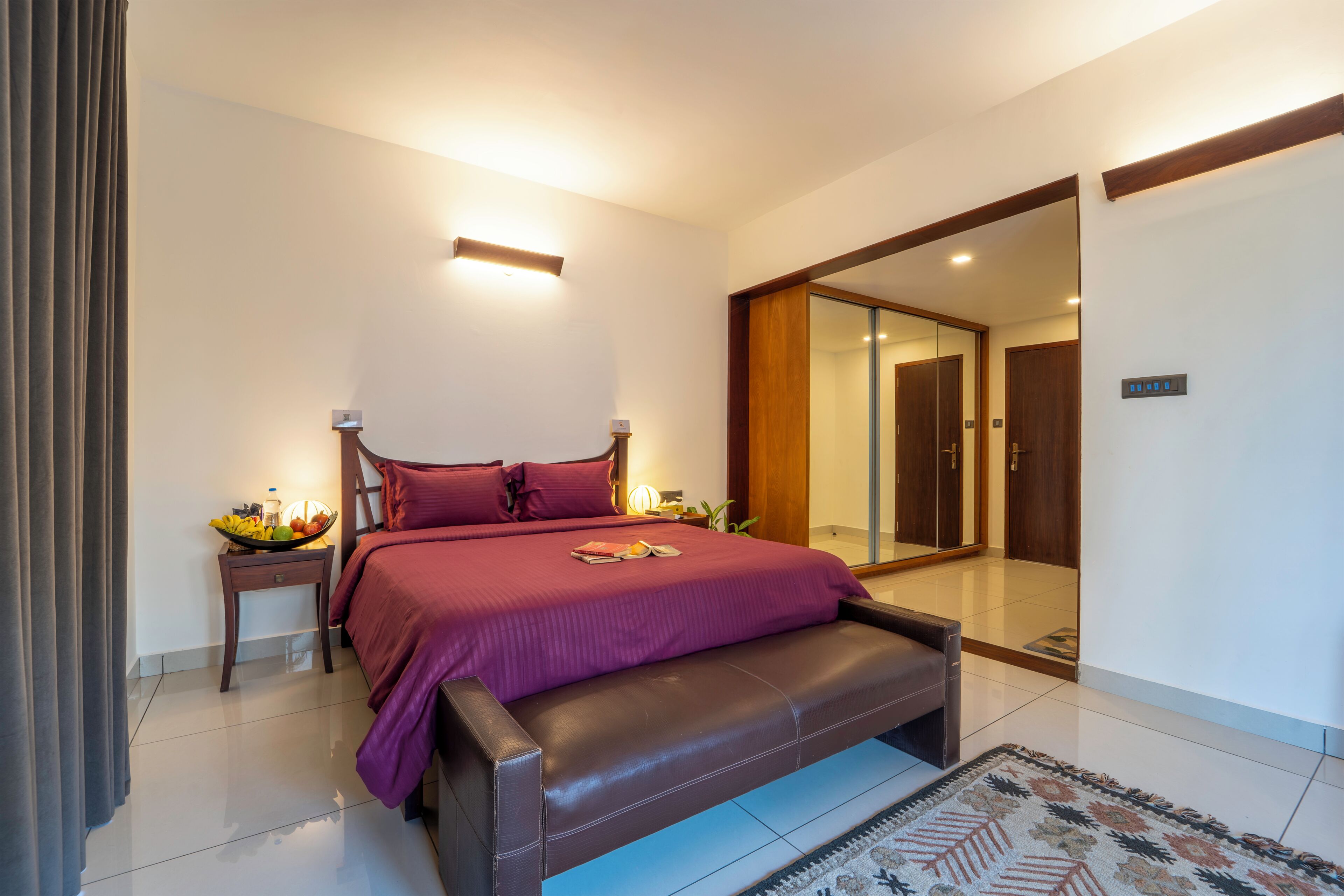A modern bedroom with a large bed, bedside tables, a mirror, and a view of the hallway.