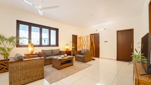 A modern living room with a sofa, armchairs, a coffee table, and a TV stand. - Alara by Alaya Stays 4-BHK Apartment (Kanayannur)