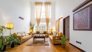 A spacious living room with a wooden floor, two sofas, a coffee table, and potted plants. - Alara by Alaya Stays 4-BHK Apartment (Kanayannur)