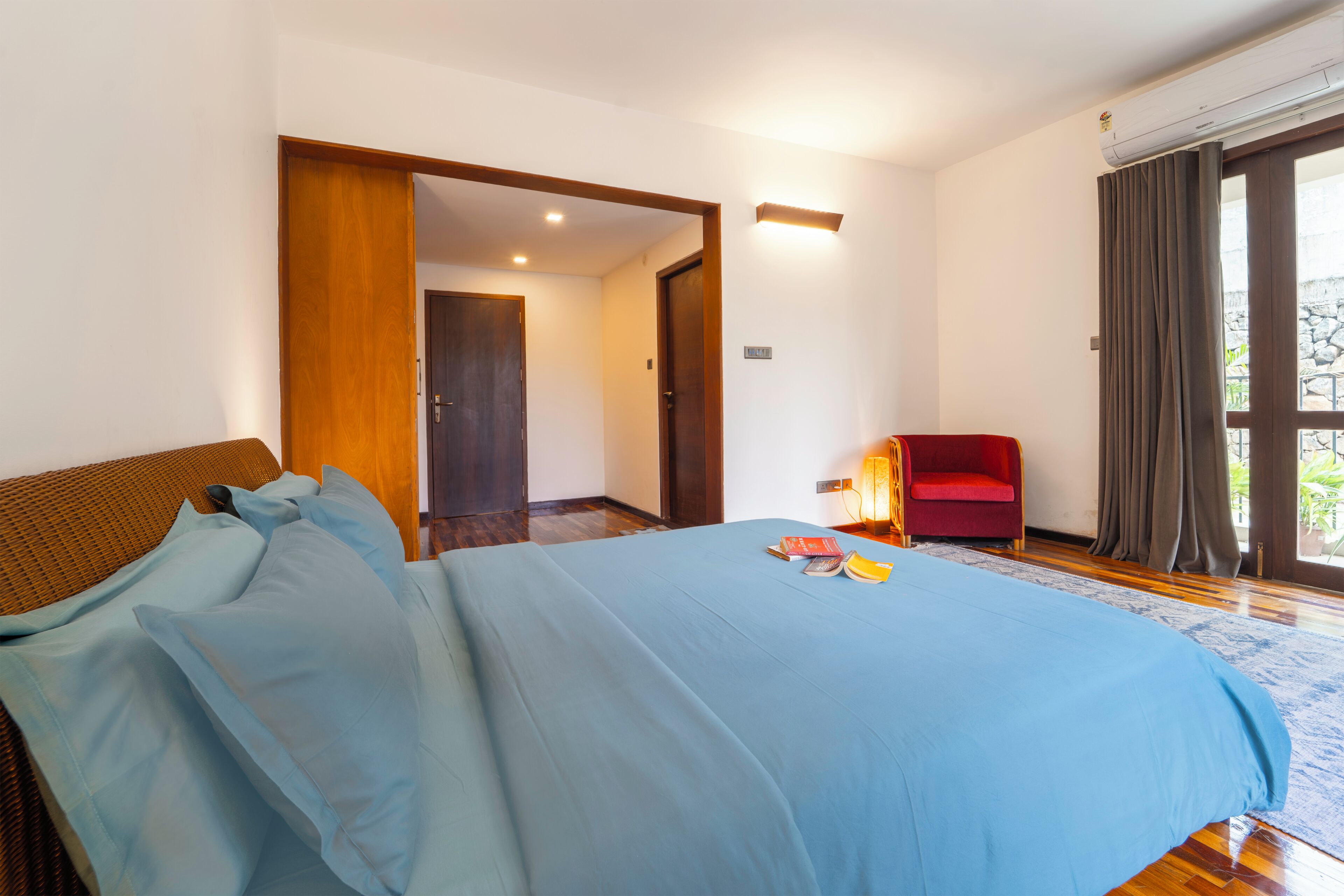 A bedroom with a bed, a red chair, and a door leading to another room.
