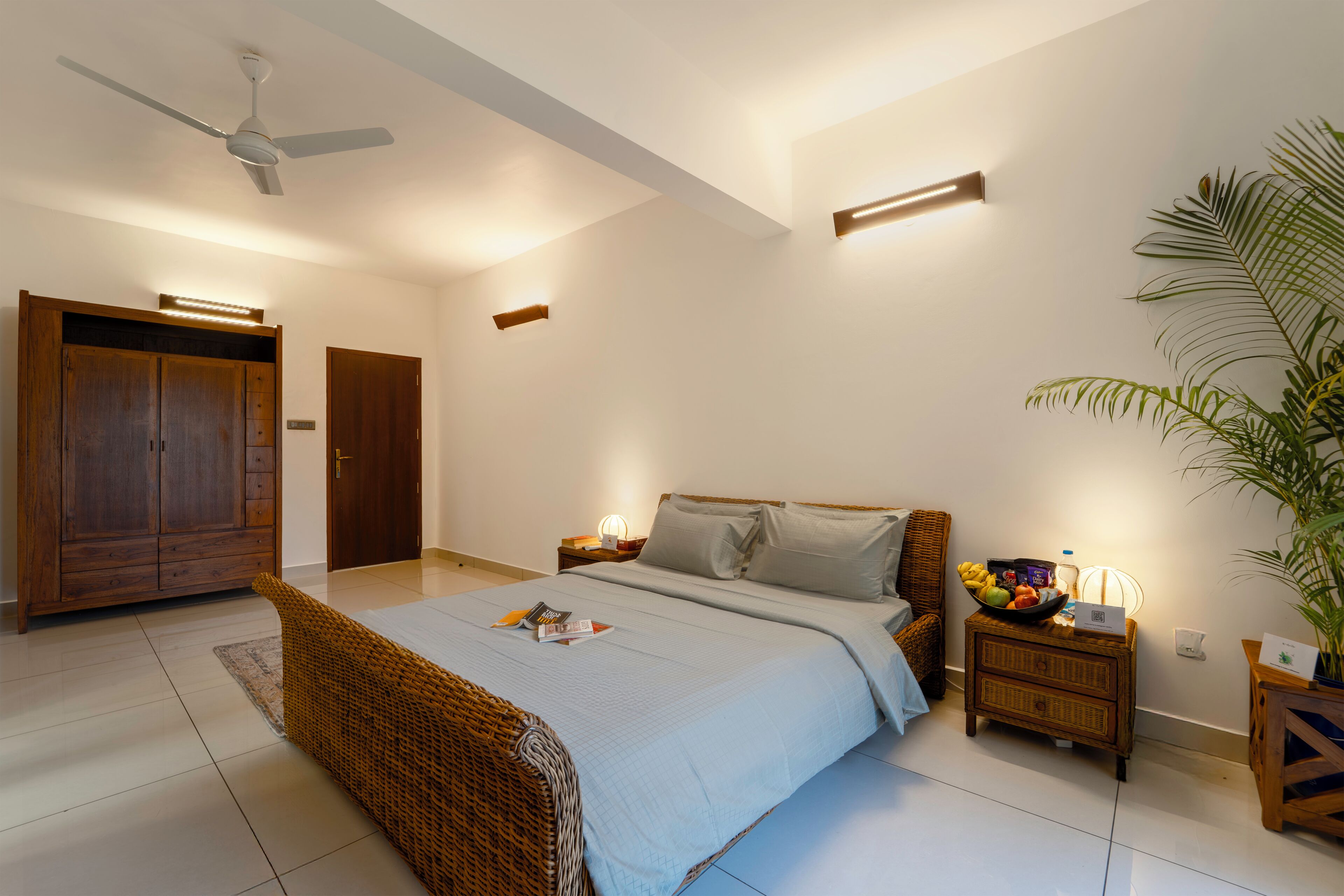 Une chambre à coucher comprenant un lit, des tables de chevet, un ventilateur de plafond, une armoire et une plante en pot.