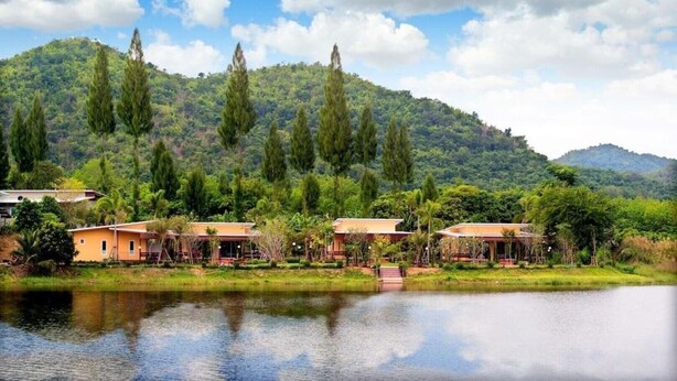 Un resort junto al lago con varias construcciones tipo bungalow, un lago tranquilo y una colina boscosa al fondo.