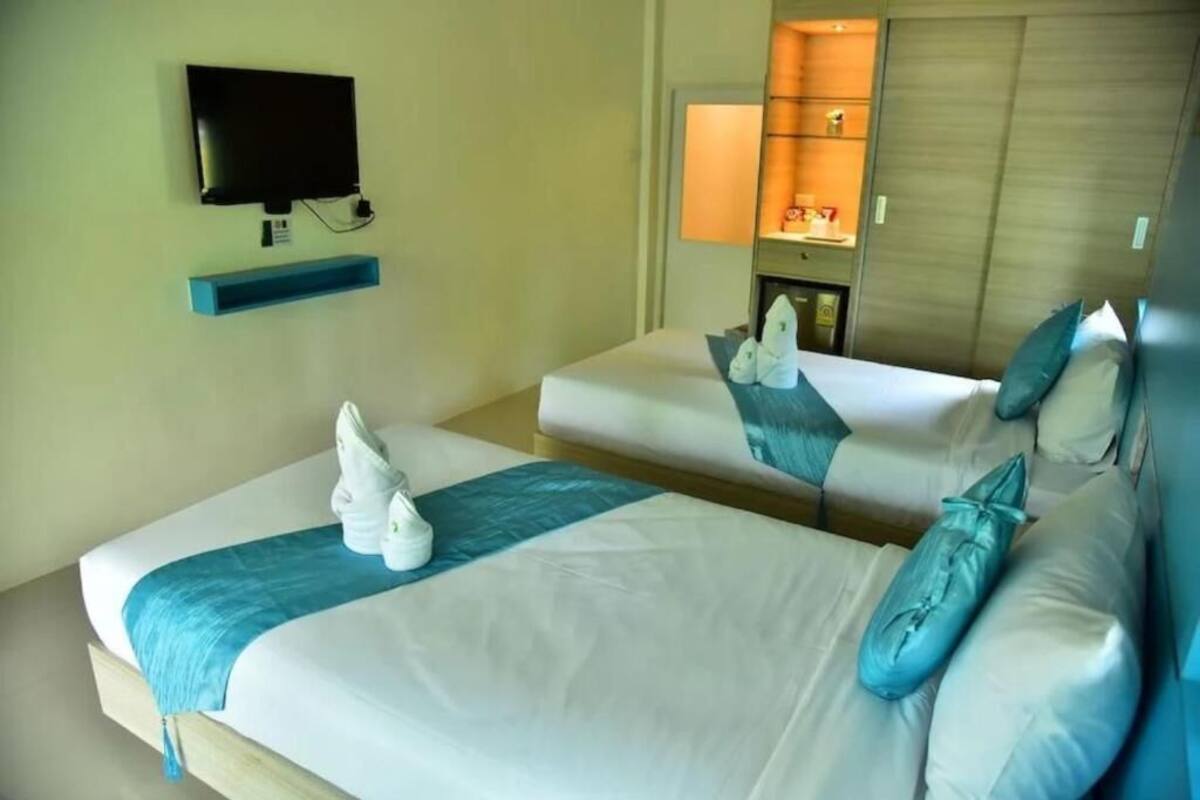 Habitación de hotel con dos camas, un televisor, una estantería y un espejo.