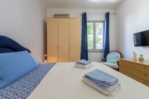 Une chambre à coucher avec un lit, une armoire en bois, une chaise, un téléviseur et une fenêtre avec des rideaux.