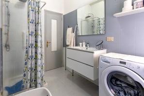 Une salle de bain Ă©quipĂ©e dâune douche, dâun lave-linge, dâun lavabo et dâun miroir.