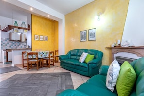 Una sala de estar con un sofá verde, una mesa de comedor con sillas, una zona de cocina y una chimenea.