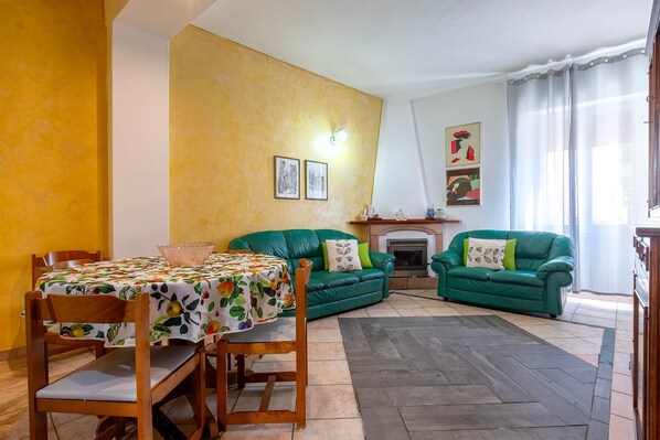 Un salon comprenant une table à manger, deux canapés verts, une cheminée et un mur jaune.