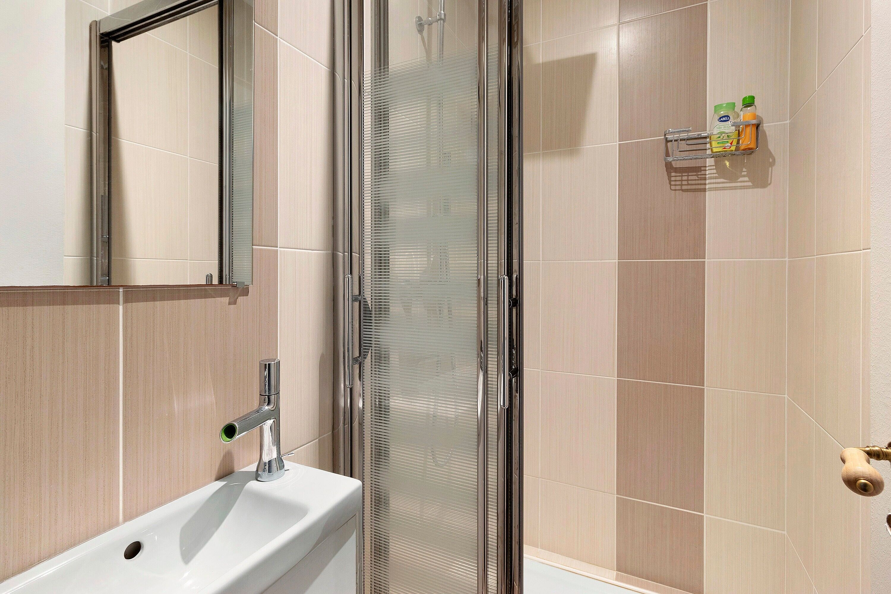 Een badkamer met een douchecabine van glas, een wastafel en een spiegel.