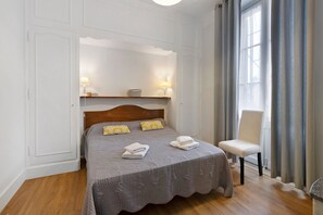 A neatly made bed with pillows, a chair, and a bedside table with a lamp. - Apartment “Hortensia” with Private Terrace and Garden (Sarlat-la-Canéda)