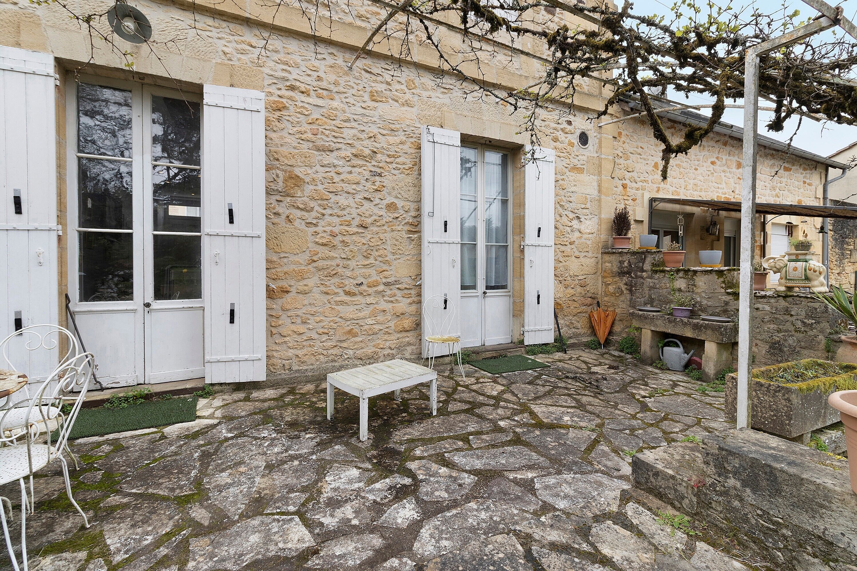Un bâtiment en pierre avec des volets blancs, une petite table et une chaise à l’extérieur.